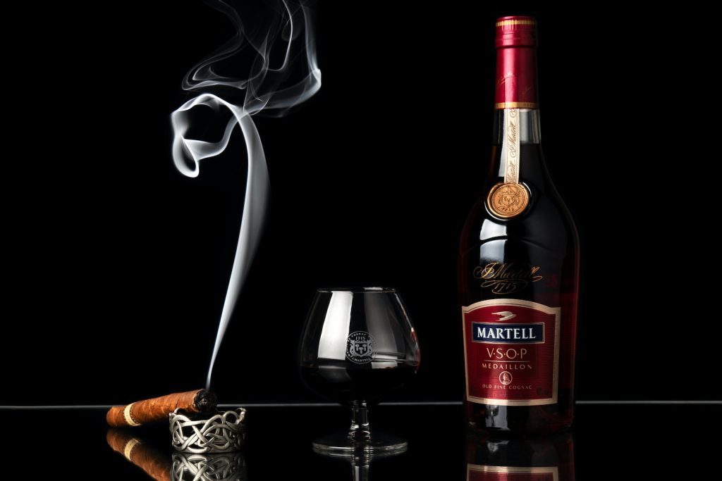 Une bouteille de whisky et un cigare à côté d'un verre.
