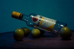Une bouteille d'alcool à côté d'un bouquet d'olives.