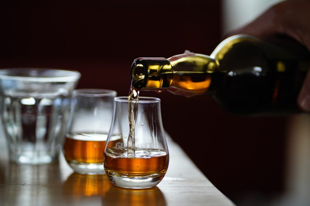 Une personne versant du whisky dans des verres sur une table.
